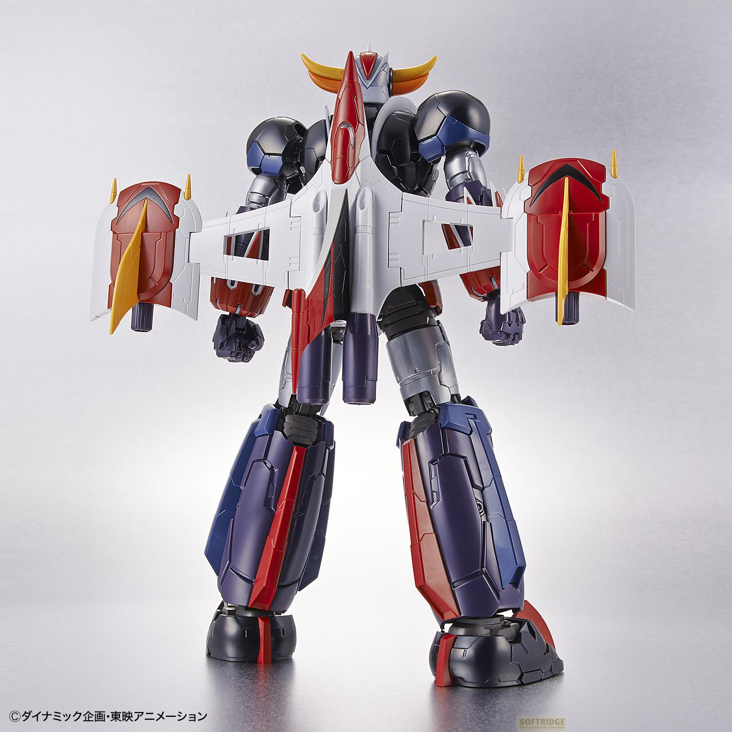 Un grand robot coloré avec des ailes et des cornes se dresse sur fond gris.