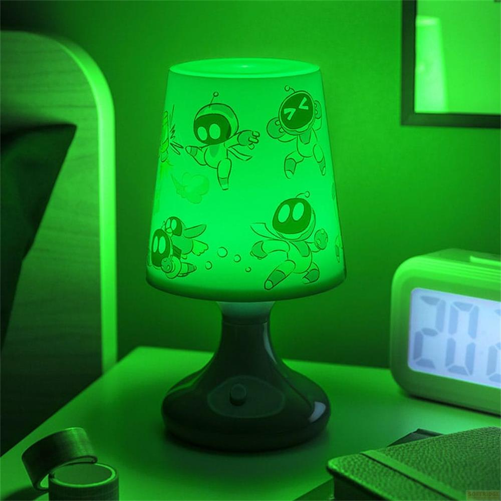 Zielona lampa z motywami astronautów na stoliku nocnym obok budzika.
