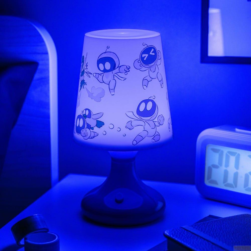 Niebieska lampa z kreskówkowymi robotami stoi na szafce nocnej obok zegara cyfrowego.