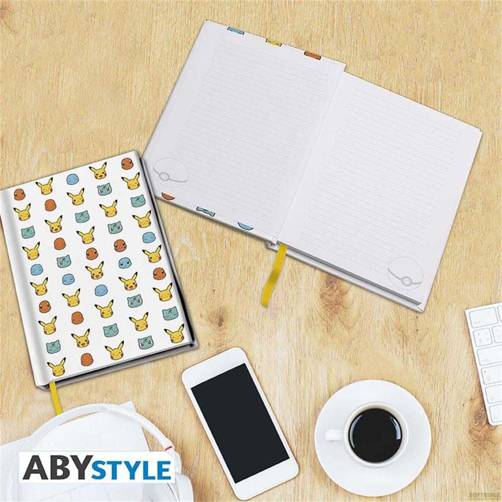 Ein Notizbuch mit Pokémon-Motiv, ein Smartphone, Kopfhörer und eine Kaffeetasse auf Holztisch.