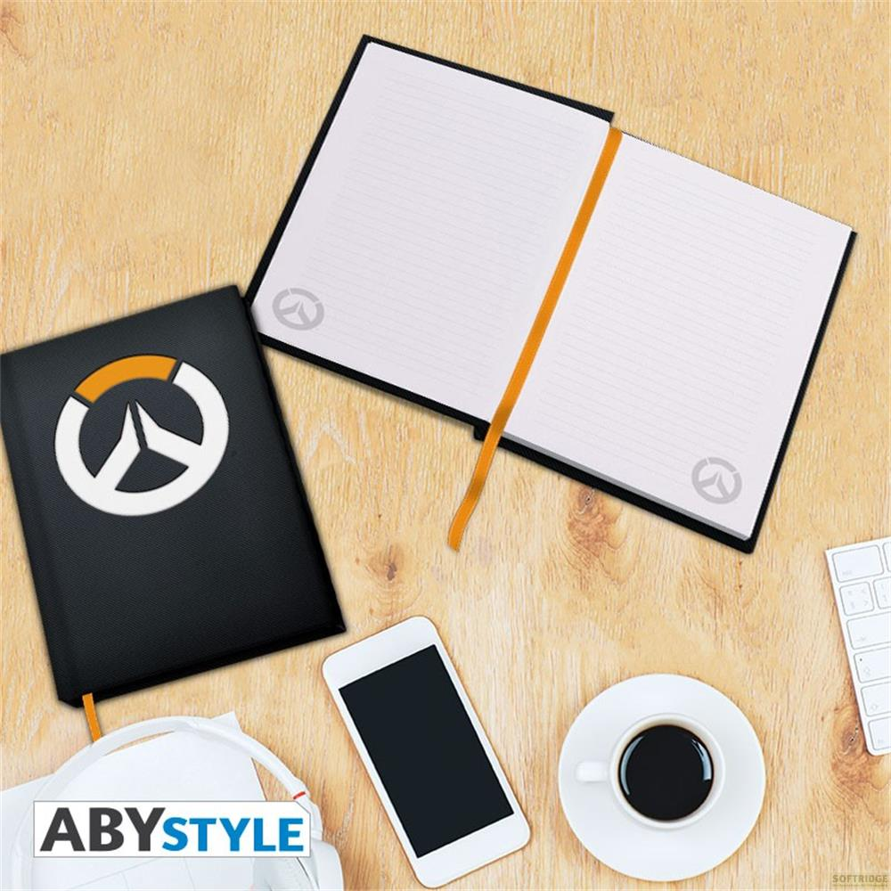Schwarzes Notizbuch mit Overwatch-Logo, daneben ein offenes Notizbuch, Handy, Kaffee.