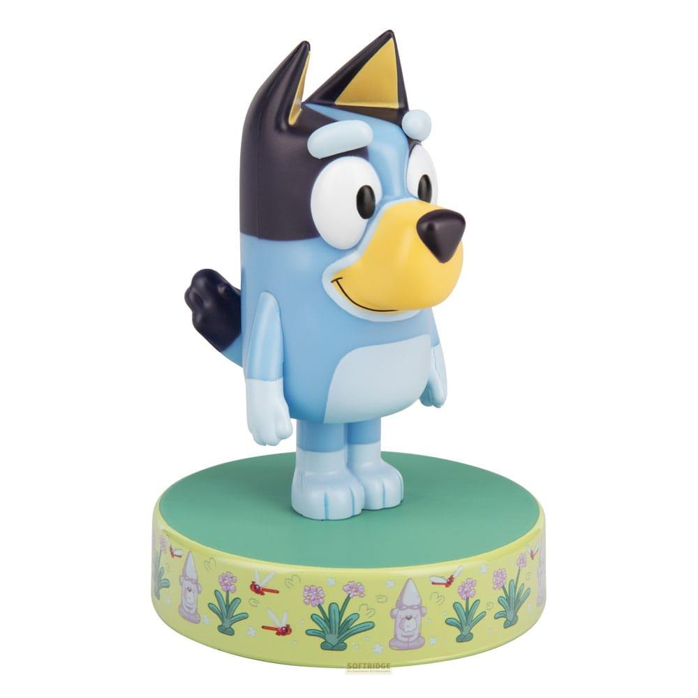 Figurka Bluey stoi na zielonej podstawie z kwiatowym wzorem. Białe tło.