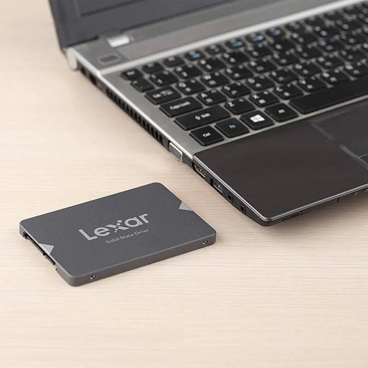 Lexar SSD neben einem offenen Laptop auf hellem Holztisch.