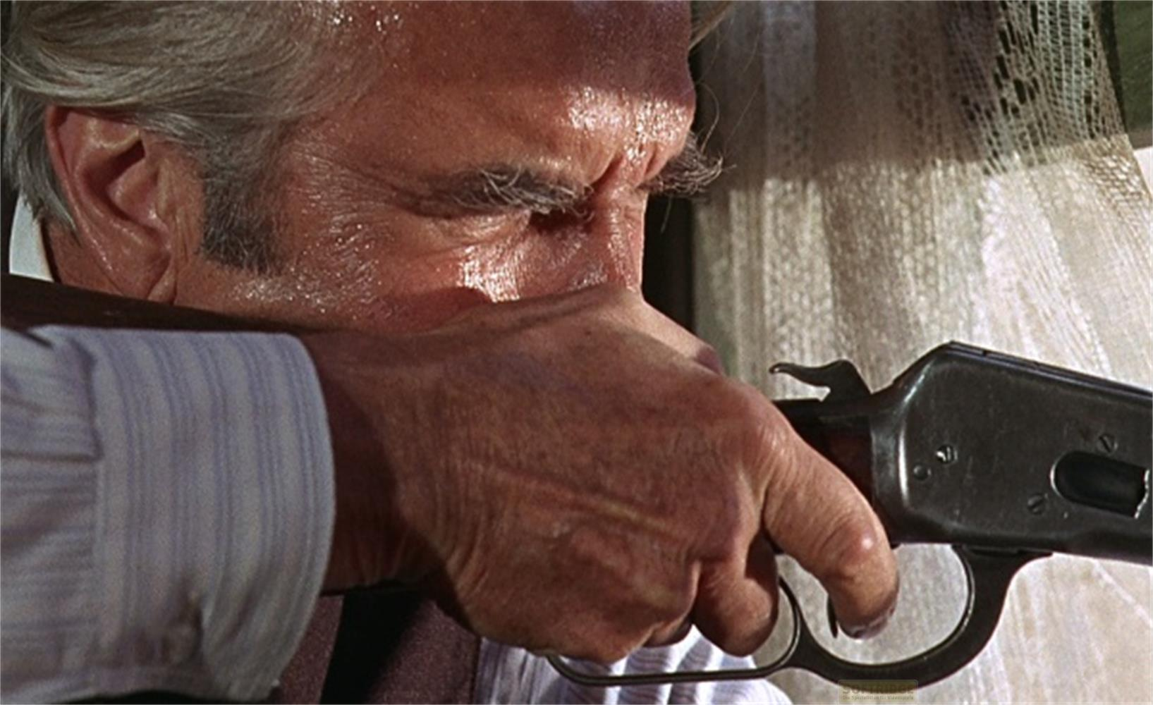 Un uomo punta un fucile, il suo viso è sudato.