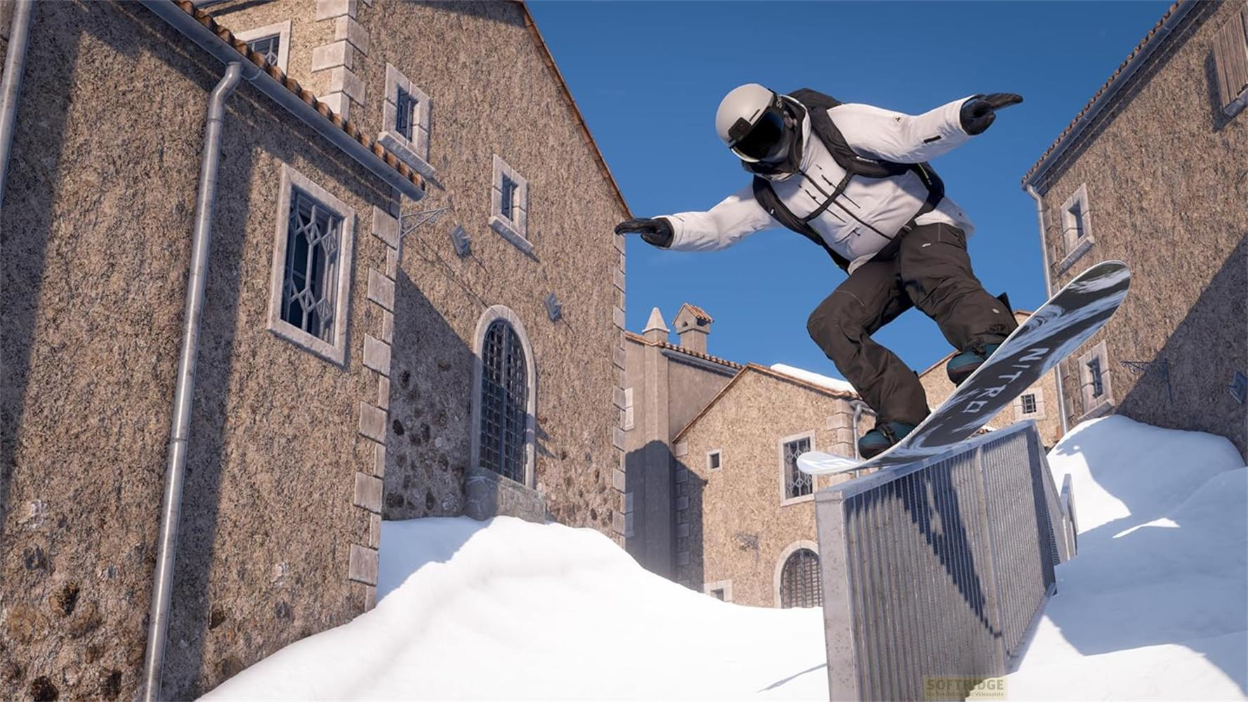 Snowboarder salta su un corrimano davanti a vecchi edifici innevati.