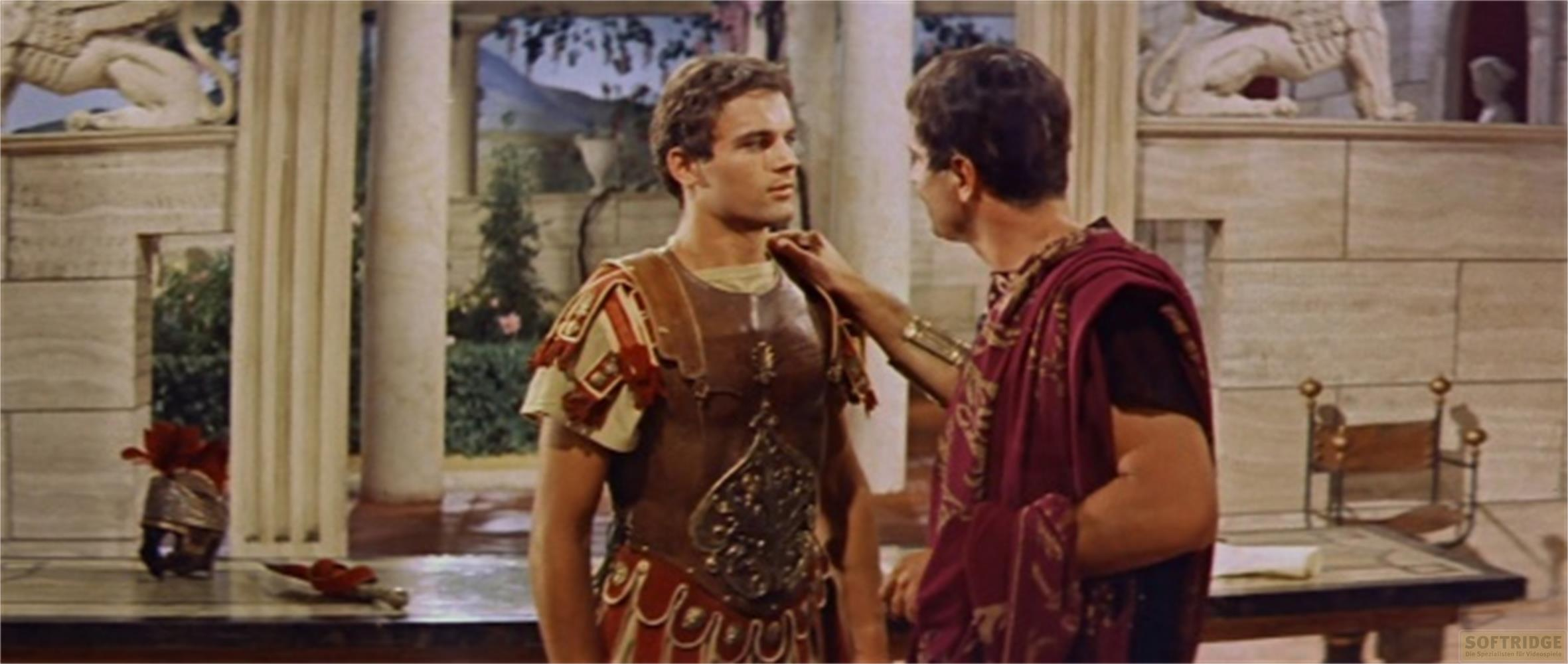 Due uomini in abiti romani si trovano in una stanza opulenta. Uno tocca la spalla dell'altro.