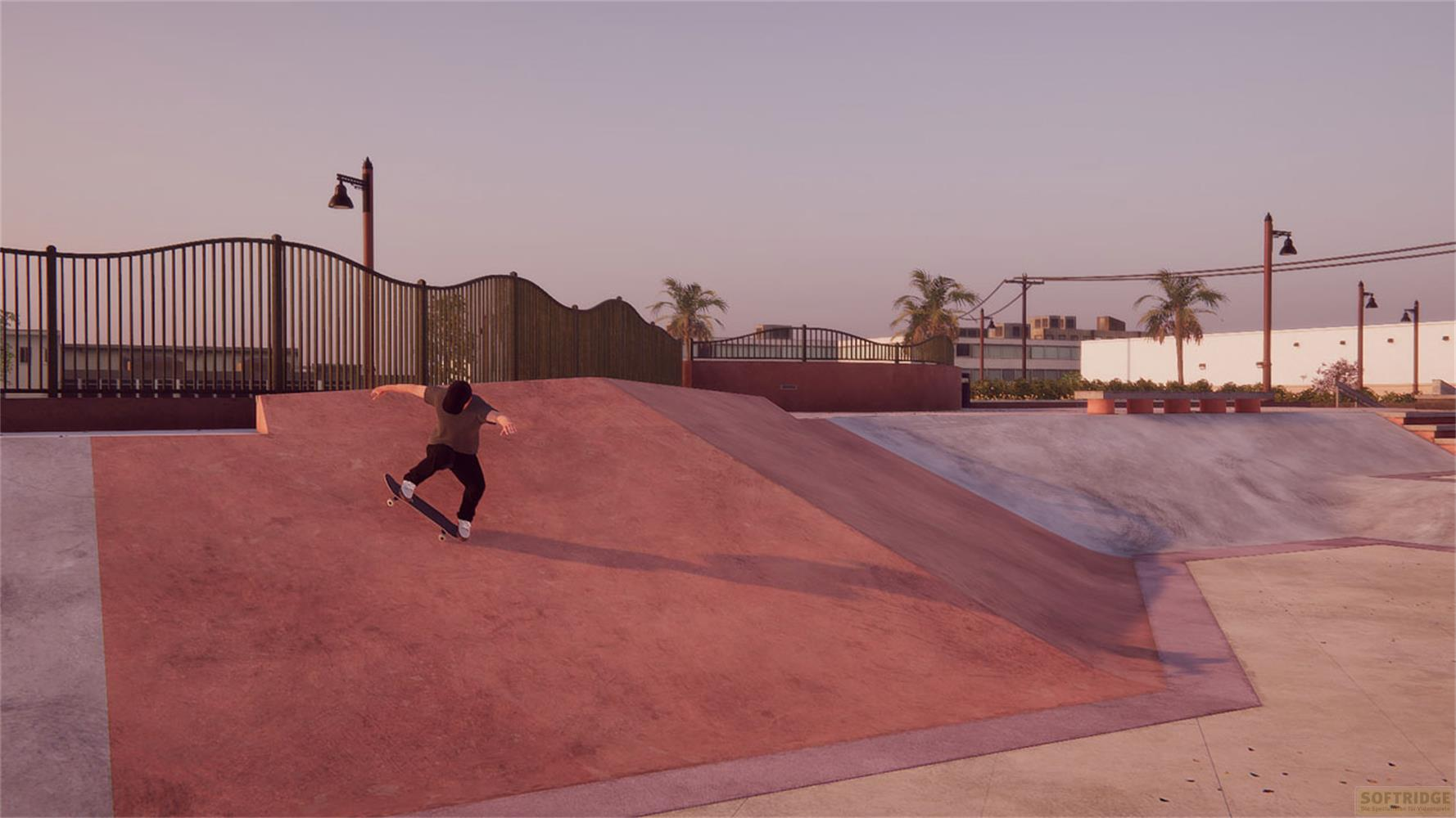 Un skateboarder descend une rampe rouge dans un skatepark au coucher du soleil.