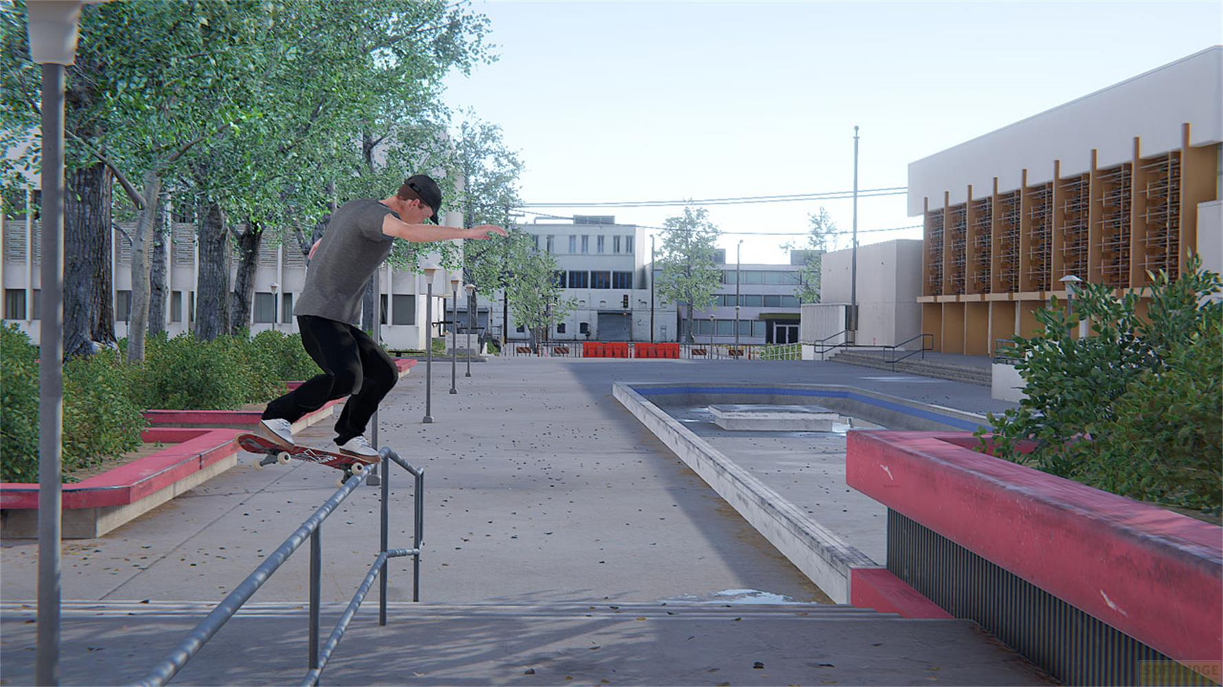 Un skateur glisse sur un rail dans un décor urbain avec des bâtiments et des arbres.