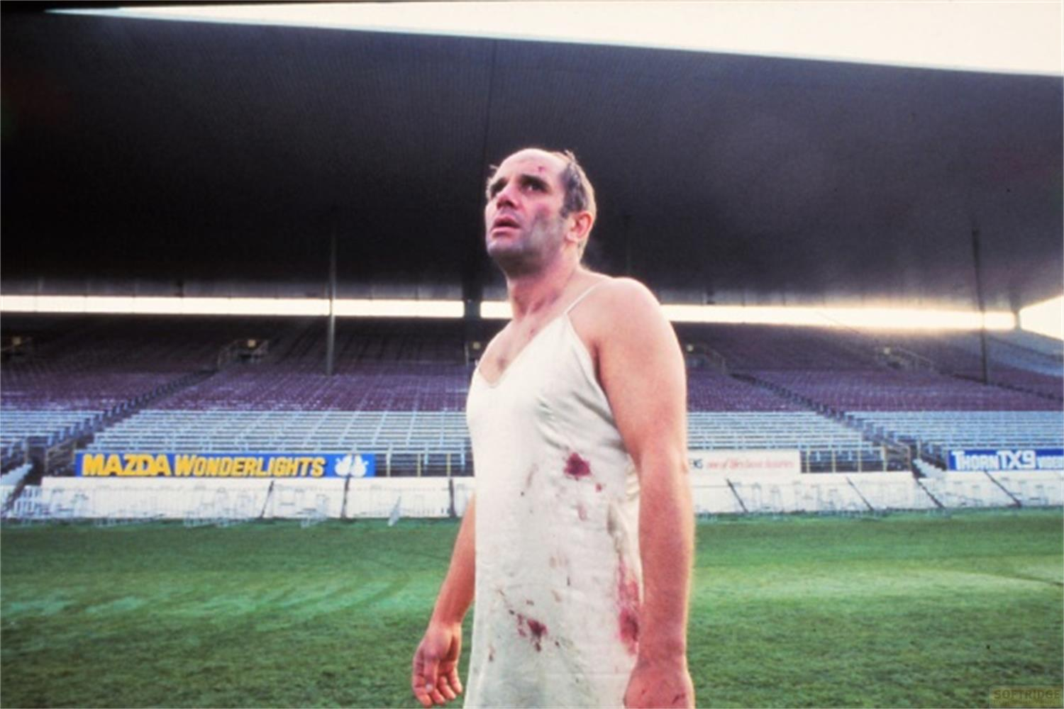 Un uomo in una sottoveste bianca con macchie di sangue su un campo sportivo.