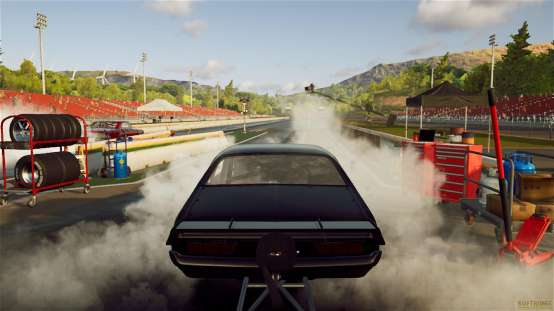 Un'auto da drag race nera parte su una pista, circondata da tribune e montagne.