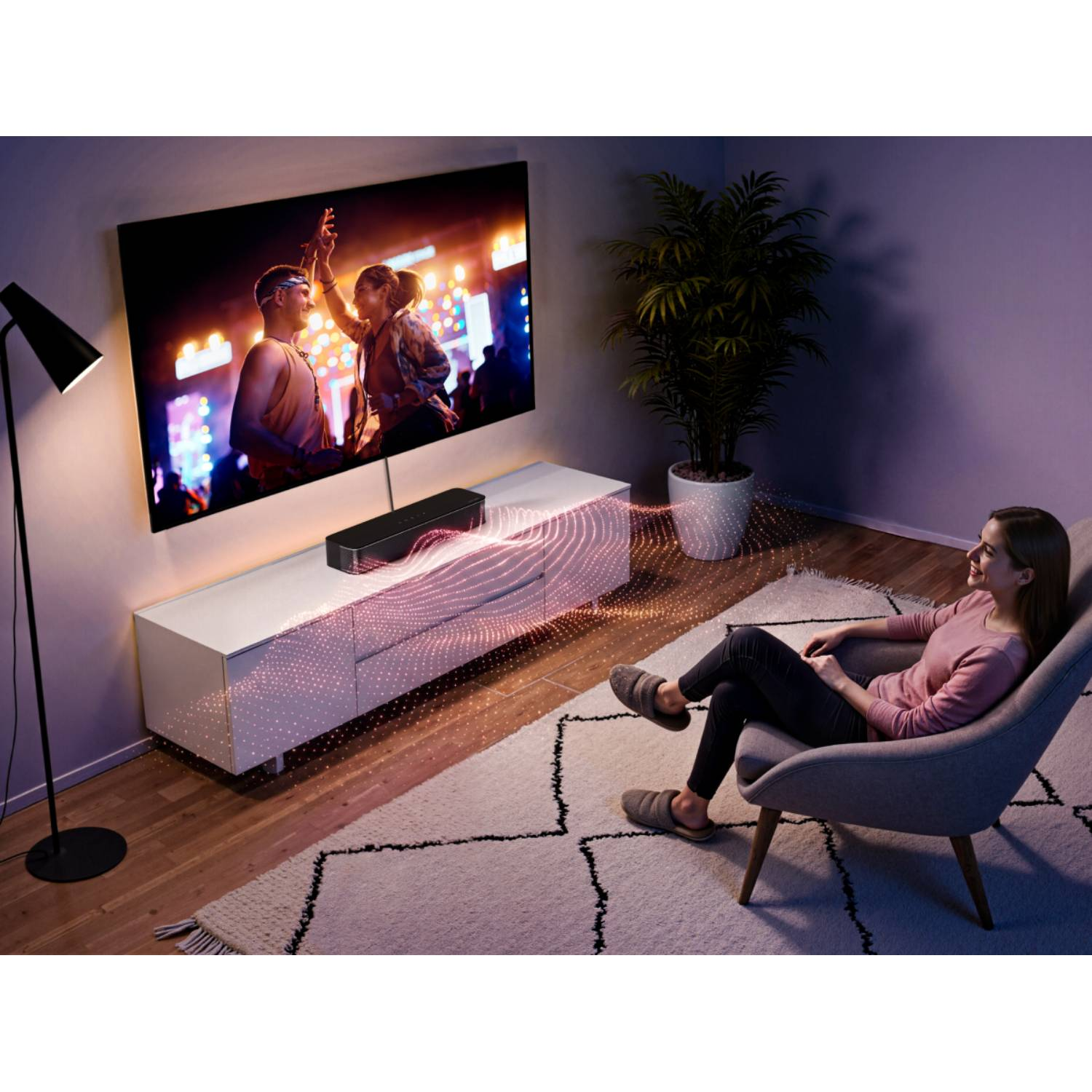 Kobieta w fotelu ogląda koncert w TV; soundbar emituje fale.