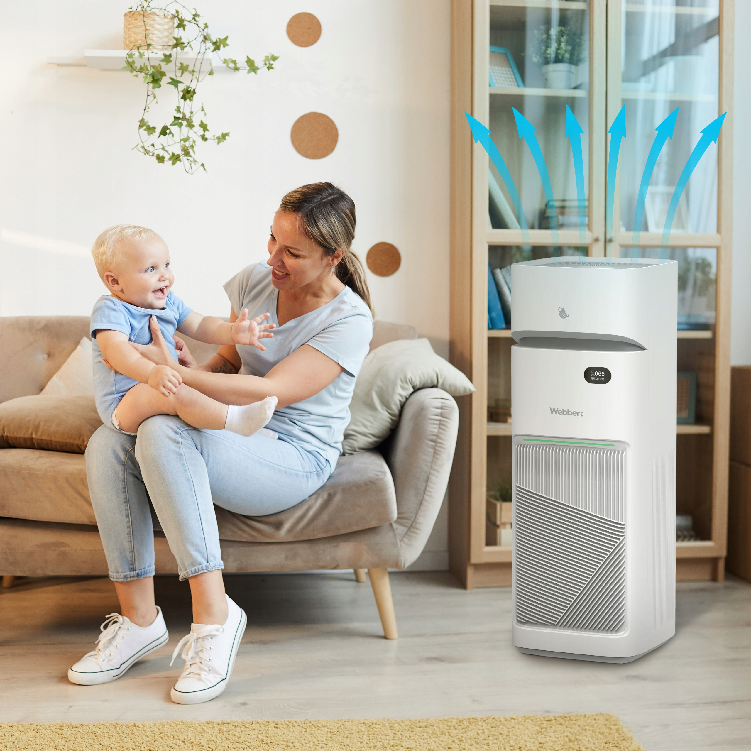 Kobieta trzyma dziecko na sofie, oczyszczacz powietrza z przodu. Niebieskie strzałki strumień.