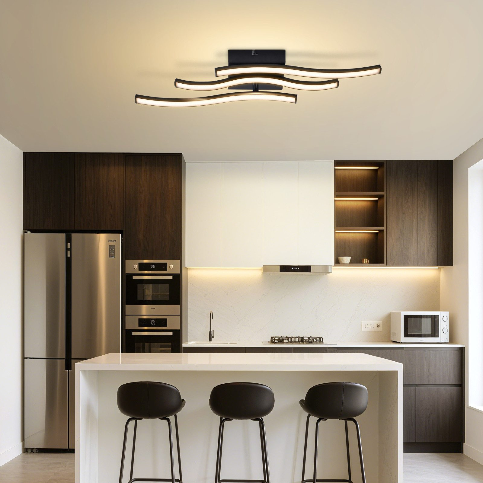 Una cucina moderna con isola, frigorifero, forni, microonde, piano cottura e sgabelli.