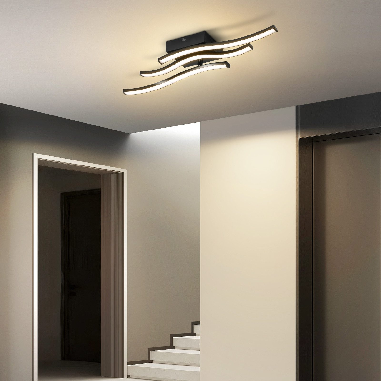 Un lampadario moderno con bracci curvi illumina un corridoio con scale.