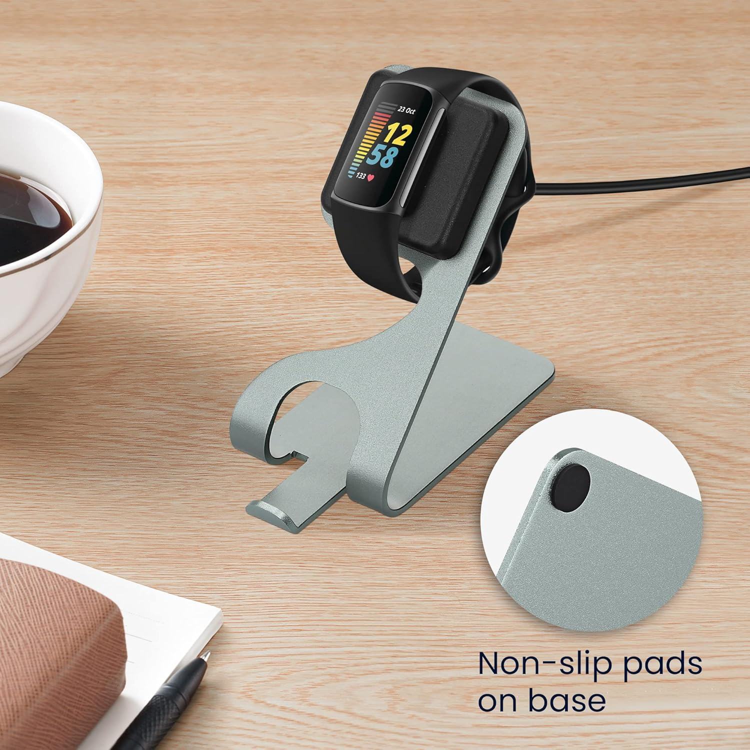 Fitness-Tracker auf Ladeständer mit Tasse Kaffee und Notizbuch.