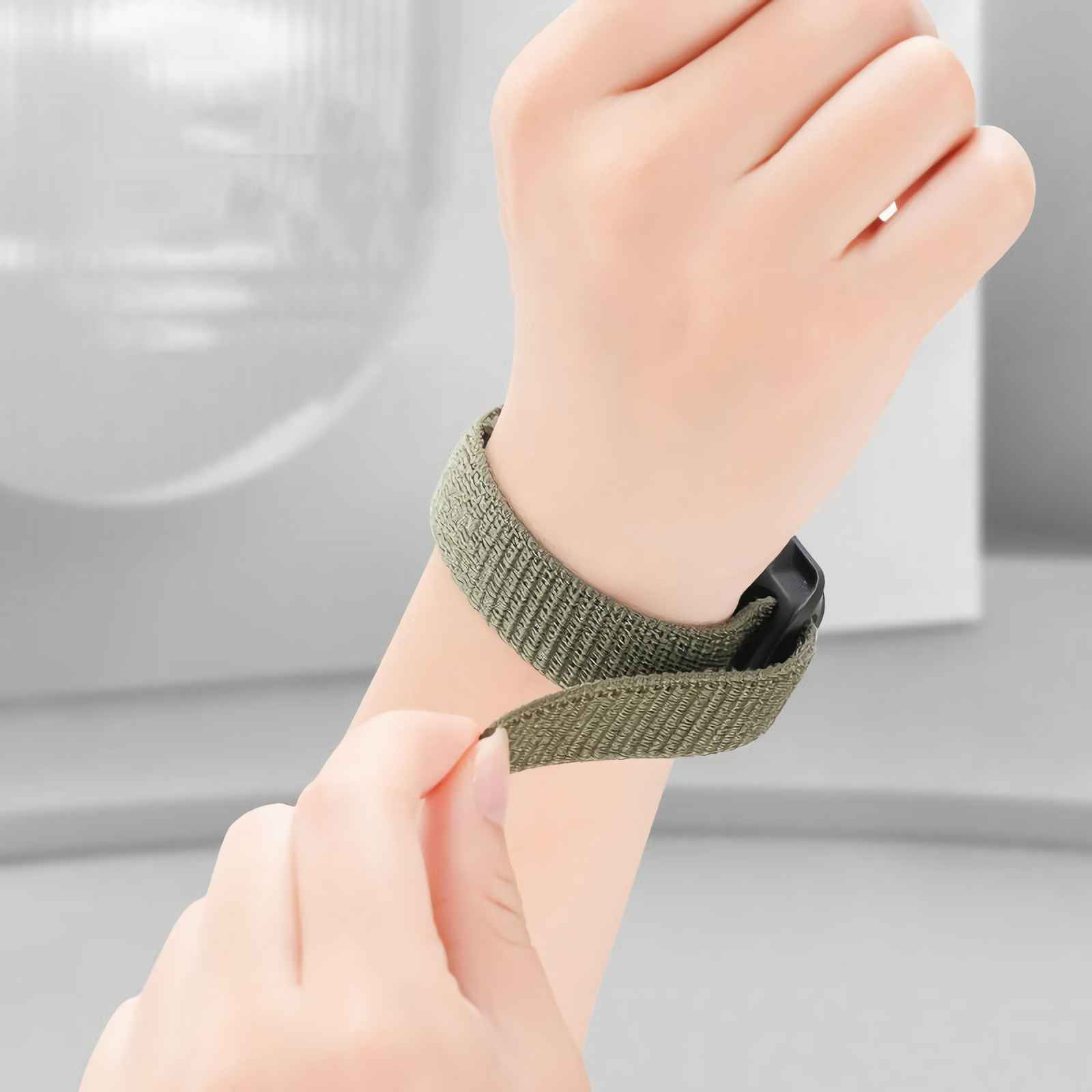 Eine Hand schließt ein olivgrünes Textilarmband um ein Handgelenk.