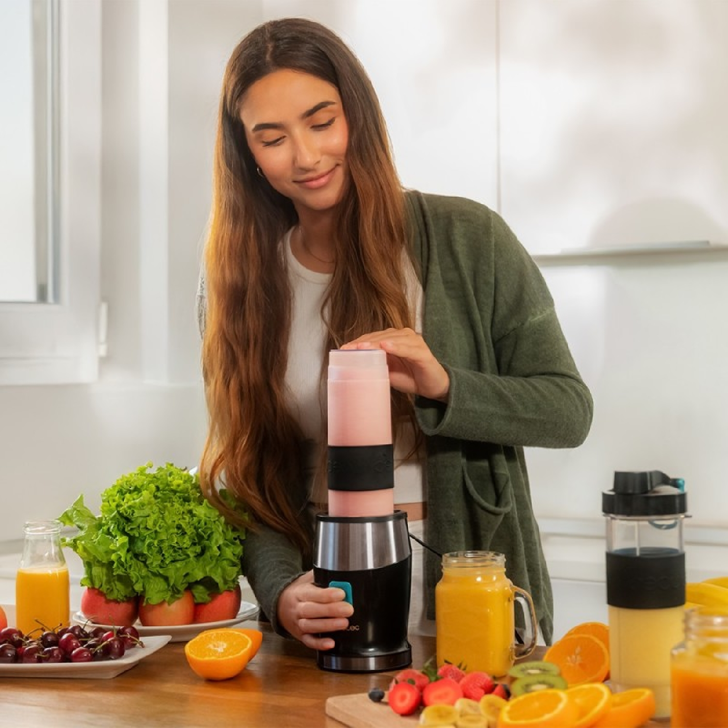Eine Frau mixt einen rosa Smoothie in einem Mixer. Obst liegt auf dem Tisch.
