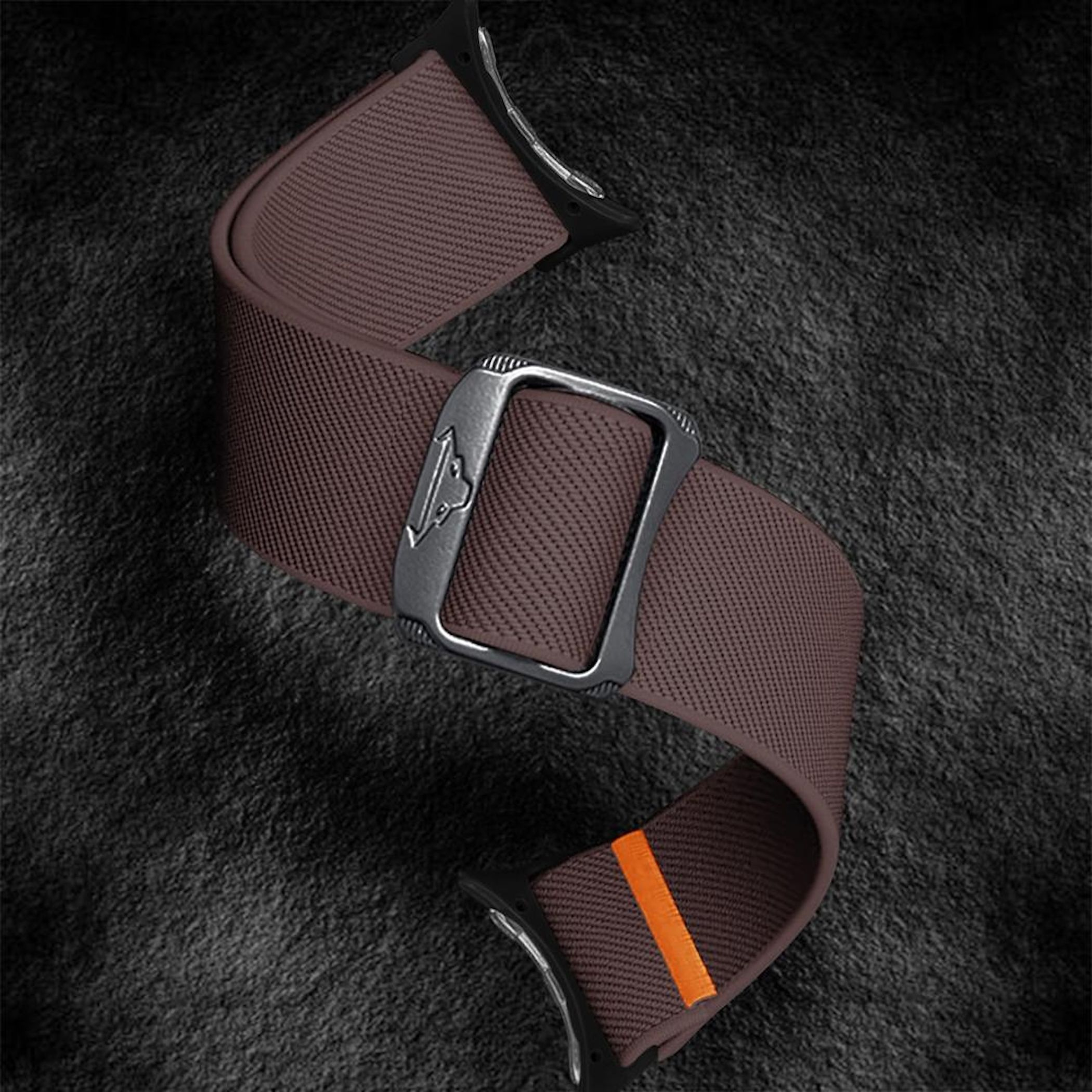 Braunes Uhrenarmband mit Silberschließe und orangefarbenem Akzent auf dunklem Grund.