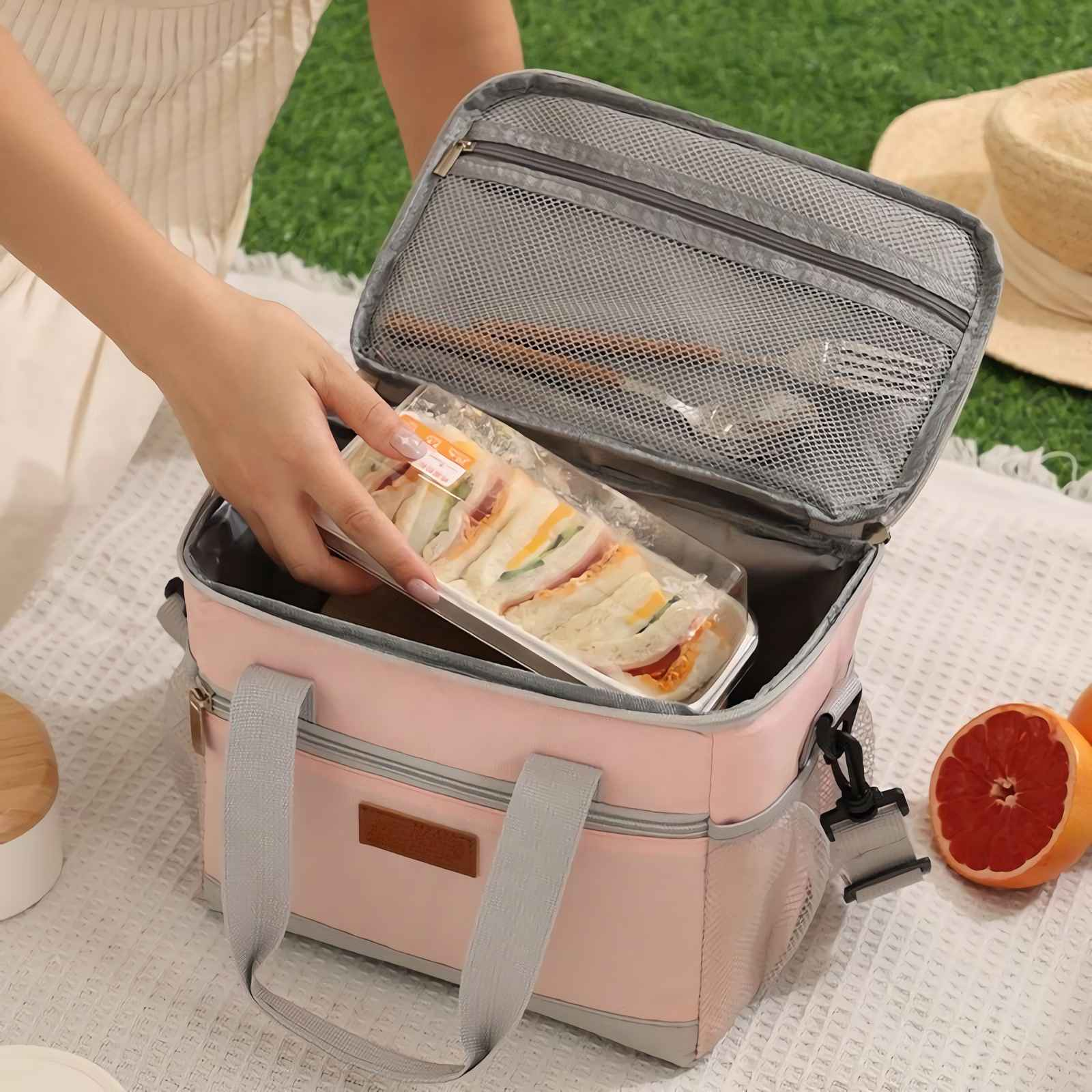 Eine Hand legt Sandwiches in eine rosa Kühltasche neben einer Grapefruit.