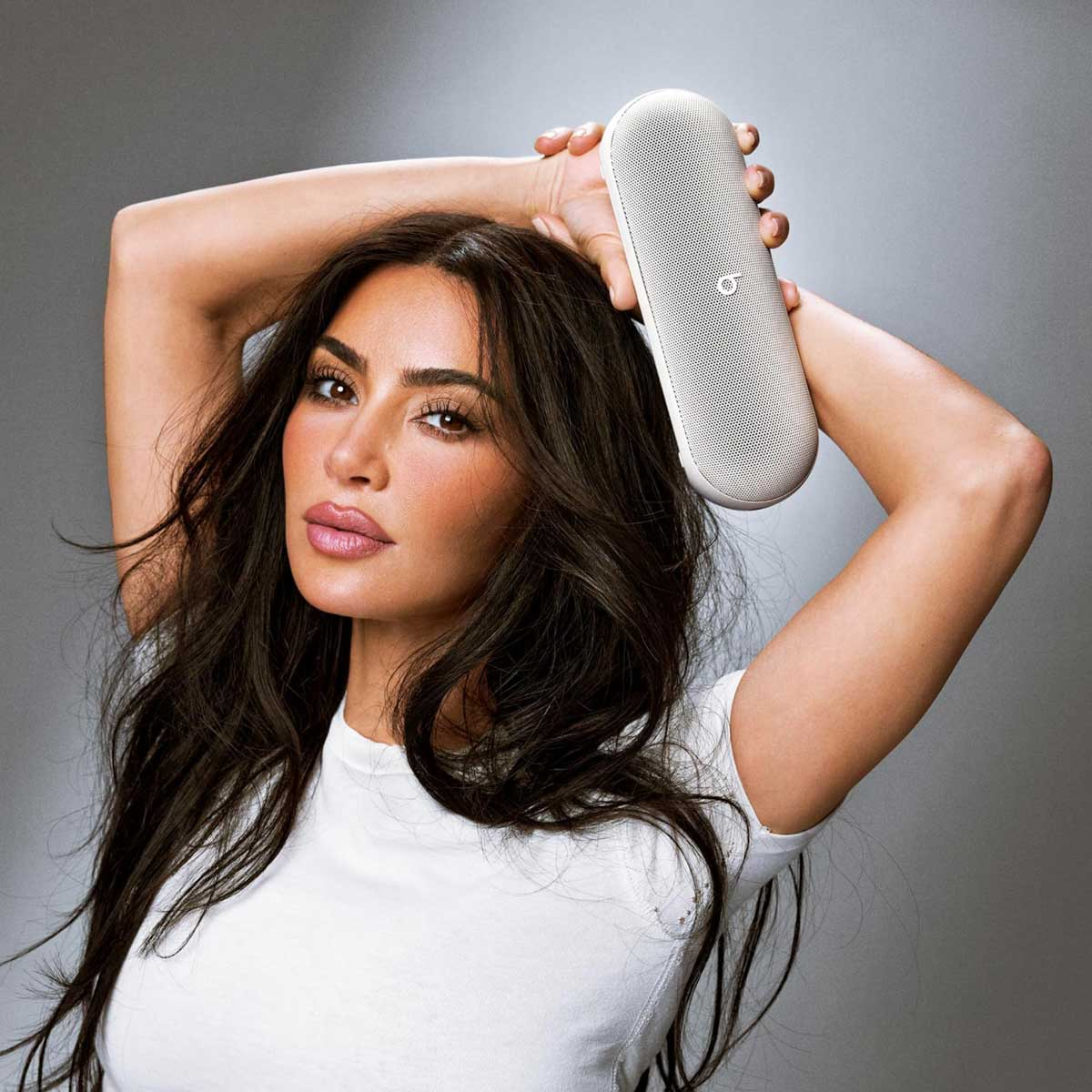 Een vrouw met lang donker haar houdt een witte luidspreker boven haar hoofd.