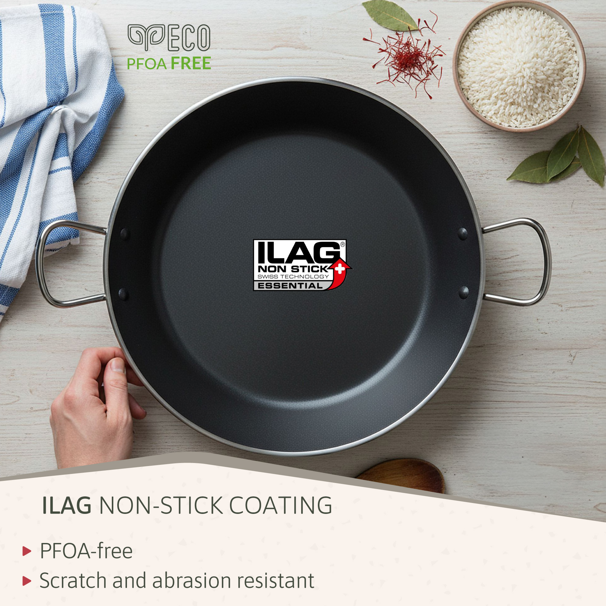 Una sartén negra ILAG con asas, junto a arroz, azafrán y hojas de laurel.