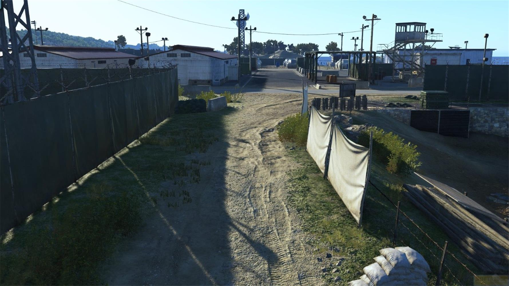 Una strada sterrata attraversa un compound in stile militare con recinzioni, edifici e una torre di guardia.