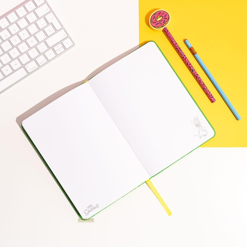 Un cuaderno abierto con un borrador de dona y bolígrafos sobre fondo amarillo y blanco.