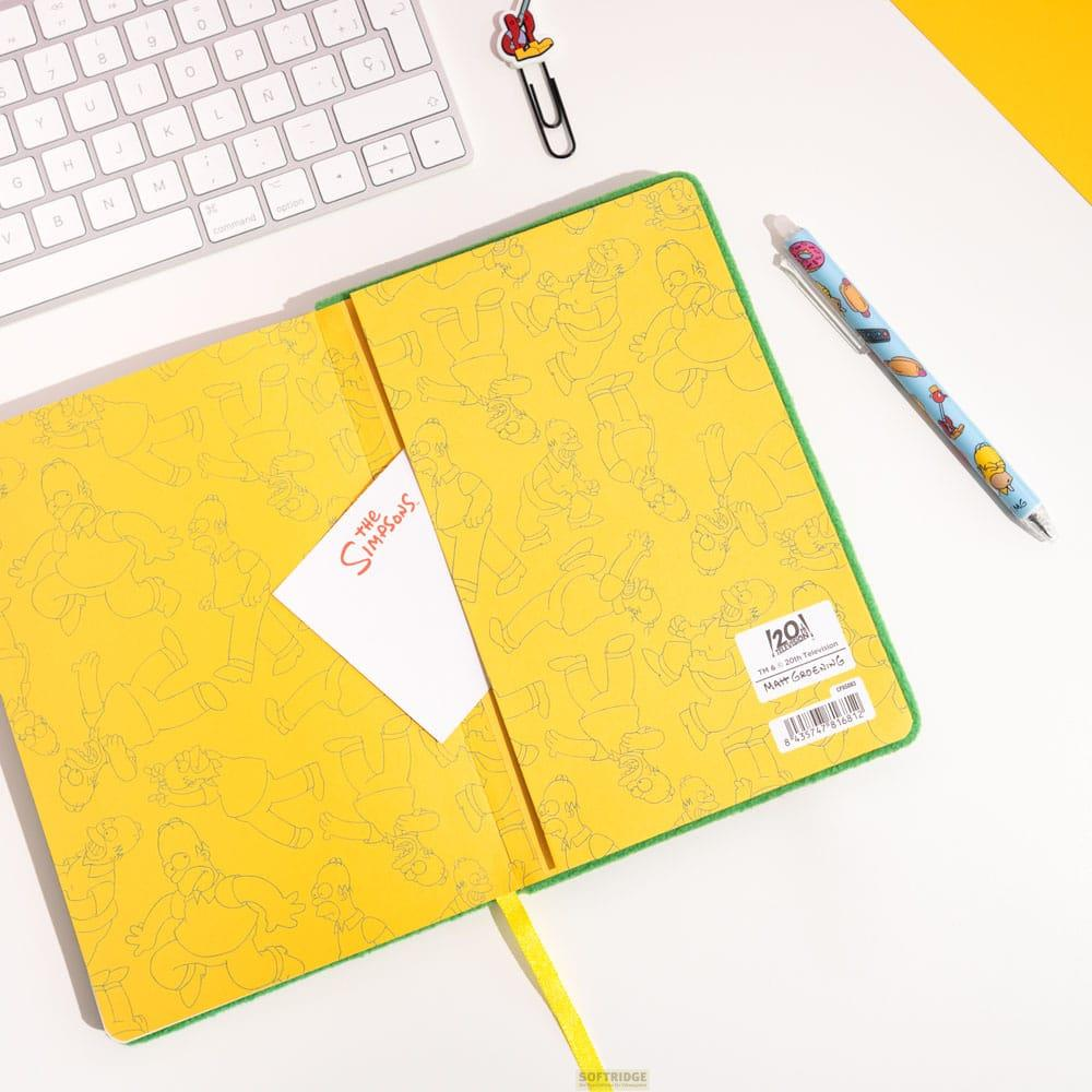 Un cuaderno abierto con motivos de Los Simpsons, bolígrafo, teclado y clip.