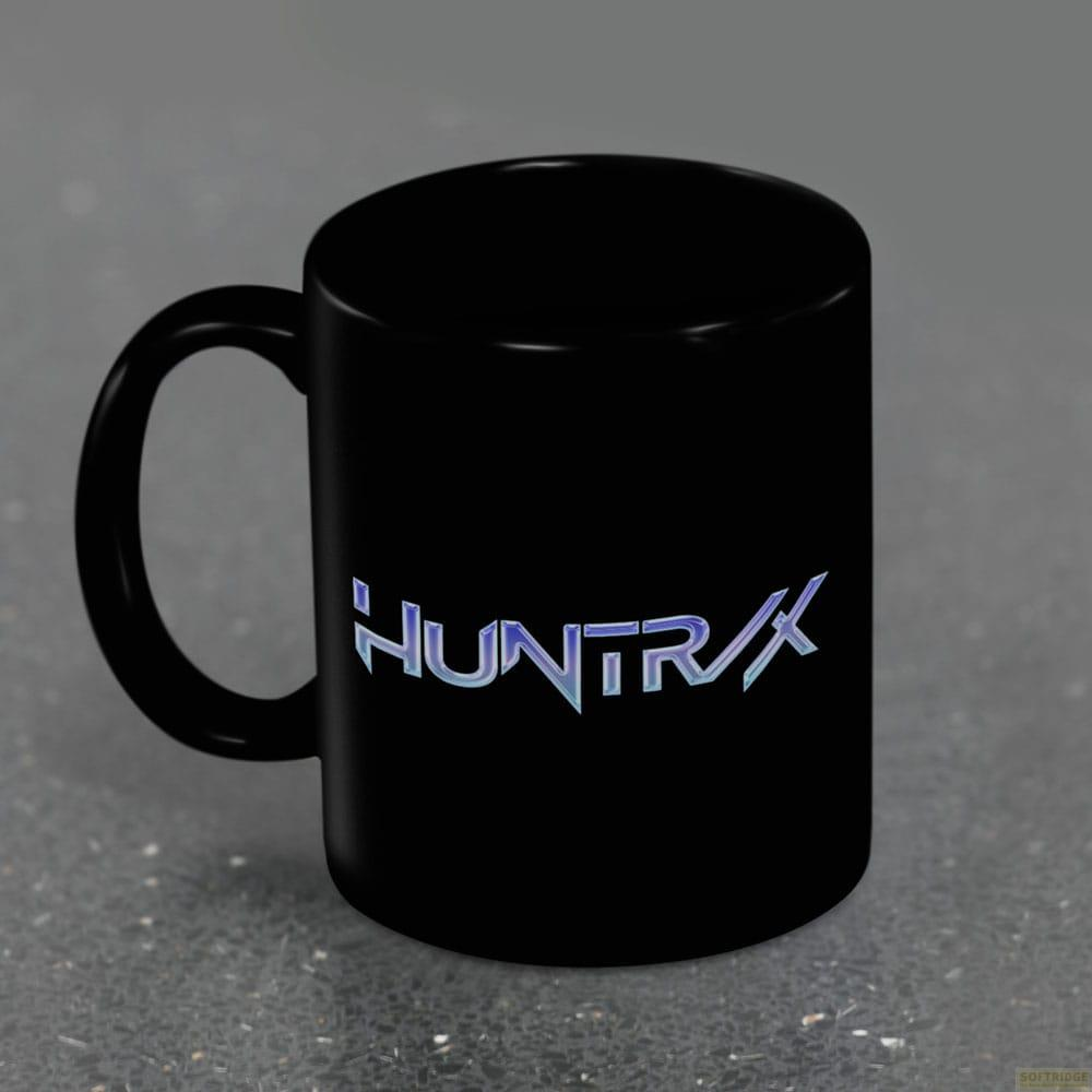 Taza negra con el texto HUNTRX en azul metálico, sobre una superficie gris.