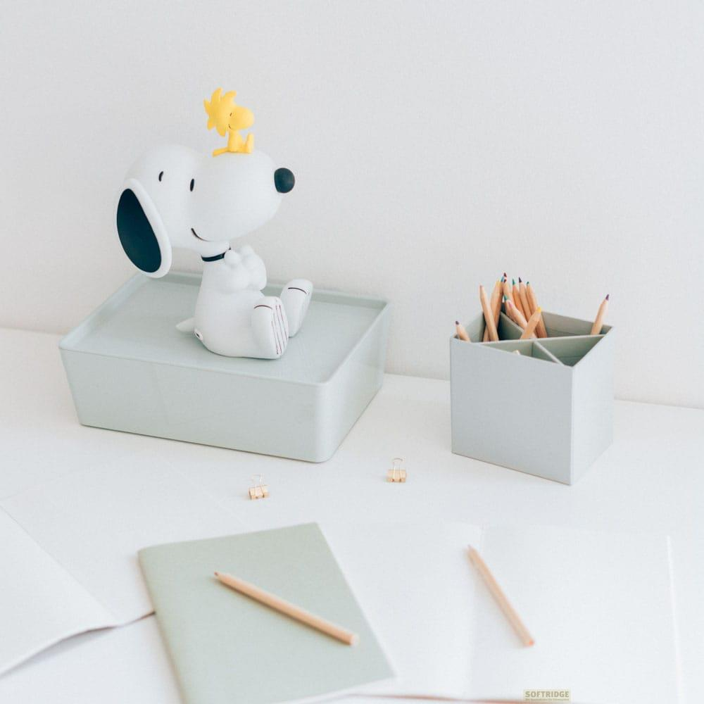 Figura de Snoopy sobre una caja verde claro, con lápices de colores en un portalápices y cuadernos.