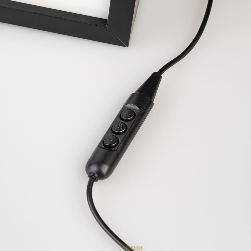 Controlador de auriculares negro con tres botones, cerca de la esquina de un marco negro.