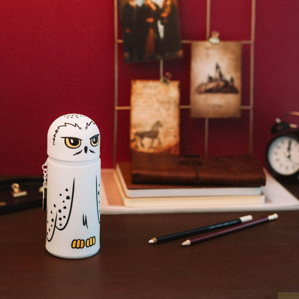Un recipiente blanco con forma de búho y ojos amarillos se sienta en un escritorio junto a lápices y libros.