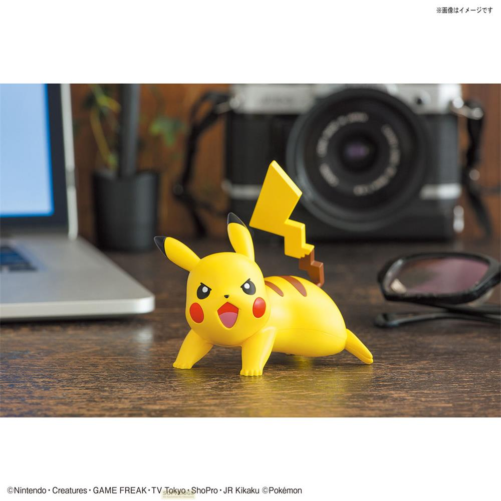 Une figurine de Pikachu se tient sur un bureau en bois devant un appareil photo et un ordinateur portable.