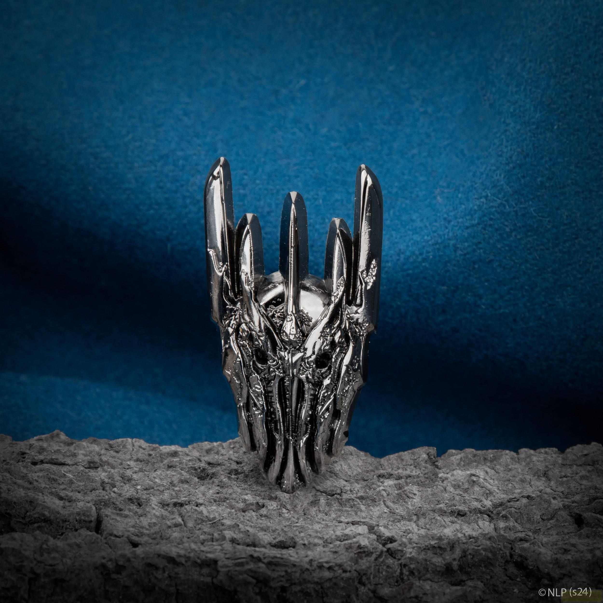 Un anillo plateado con diseño de calavera sobre una superficie gris.