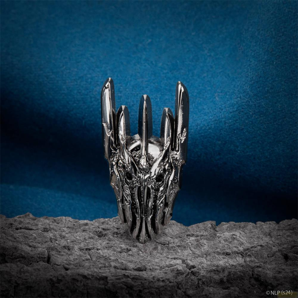 Un anillo de plata con un diseño detallado del yelmo de Sauron sobre una superficie rugosa y fondo azul.