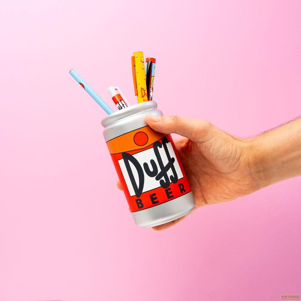 Una mano sostiene un portalápices plateado en forma de lata con marca 'Duff Beer'.