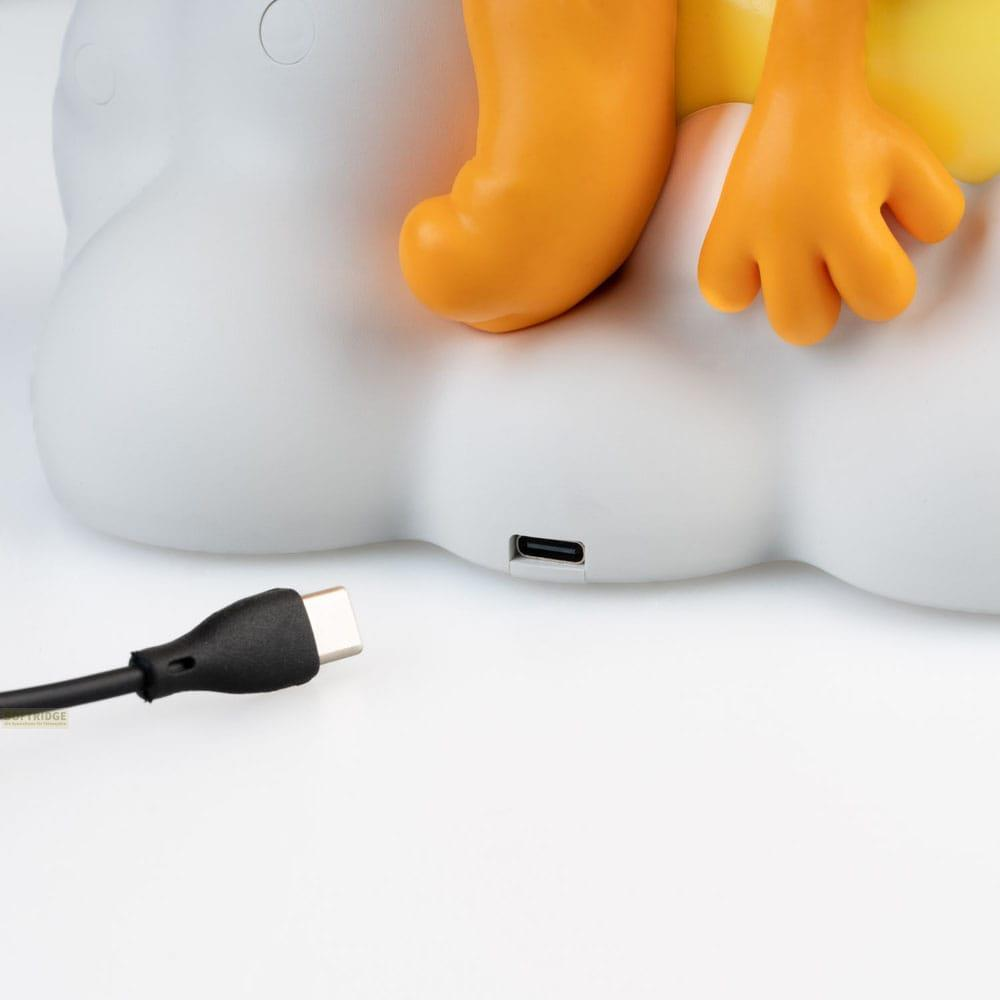 Un cable USB-C yace junto a una forma de nube blanca con pies naranjas.