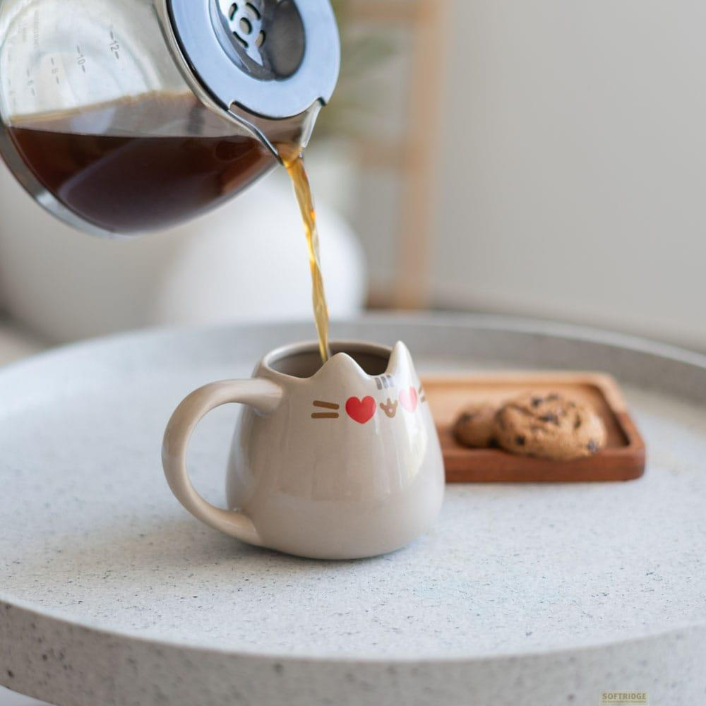 El café se vierte en una taza beige con forma de gato, con galletas cerca.
