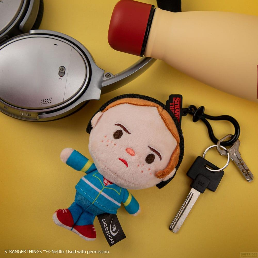 Un llavero de peluche de Stranger Things con llaves yace junto a auriculares plateados y una botella de agua amarilla.