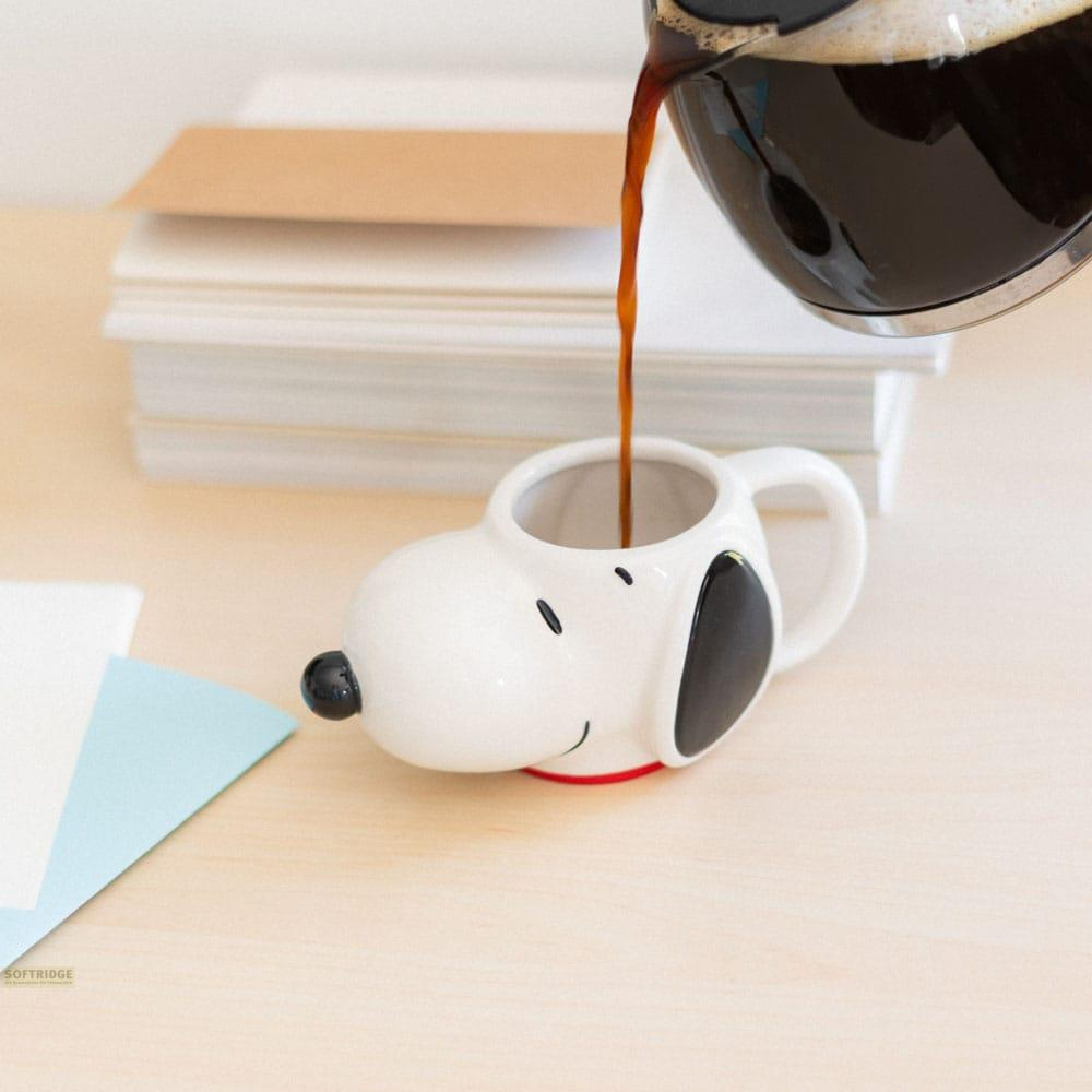 Café se vierte en una taza de Snoopy, con libros al fondo.