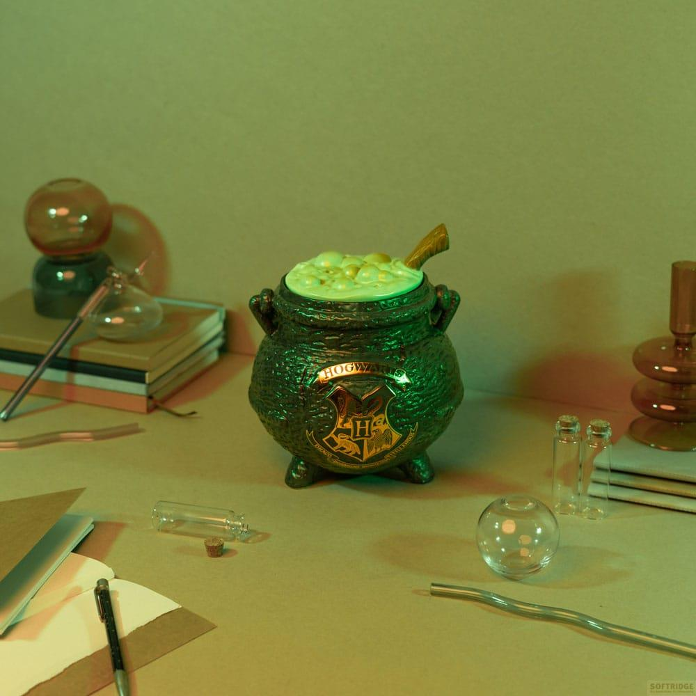 Caldero verde con escudo de Hogwarts, lleno de poción verde, sobre mesa con libros y objetos de cristal.