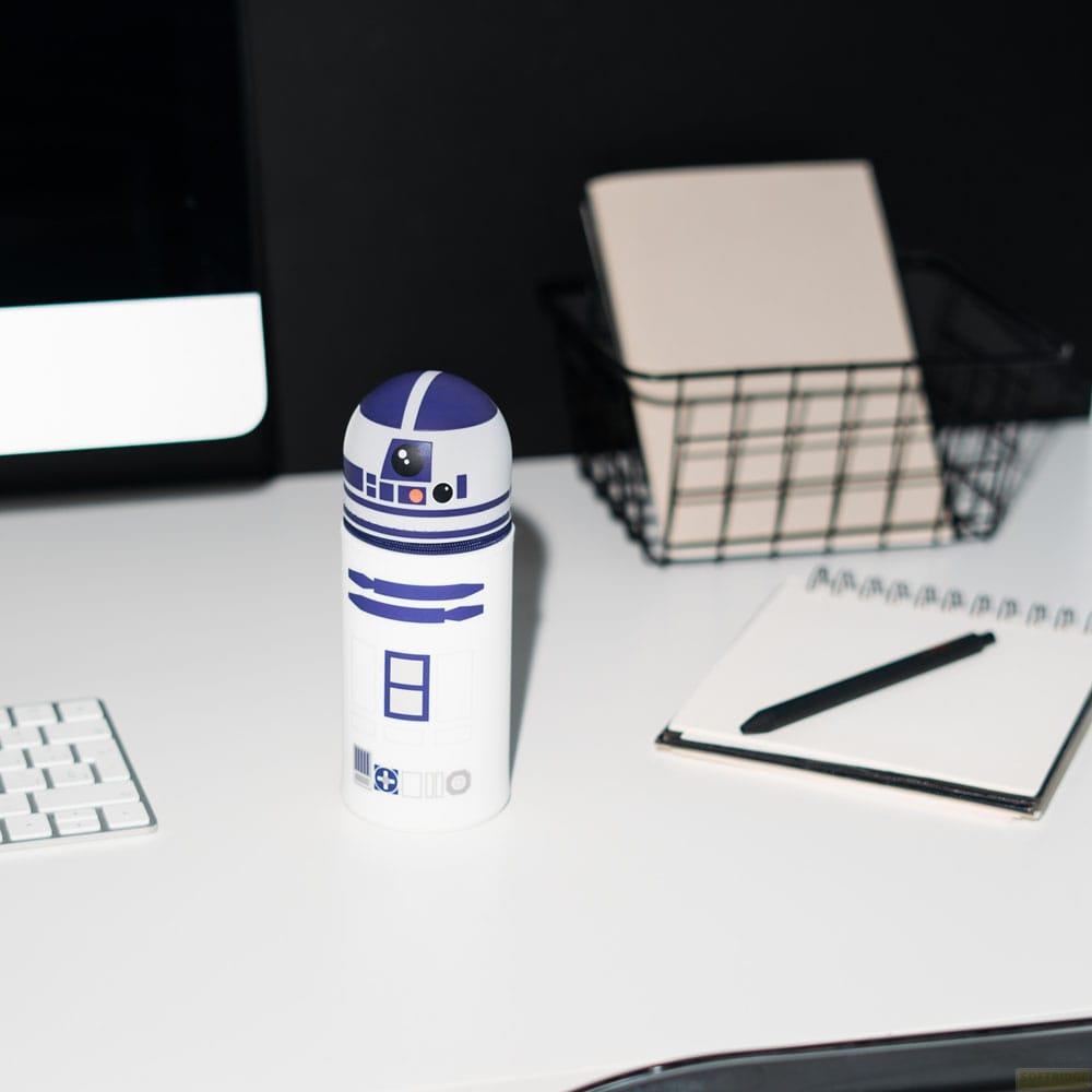 Una figura de R2-D2 está sobre un escritorio blanco junto a un cuaderno y una cesta.