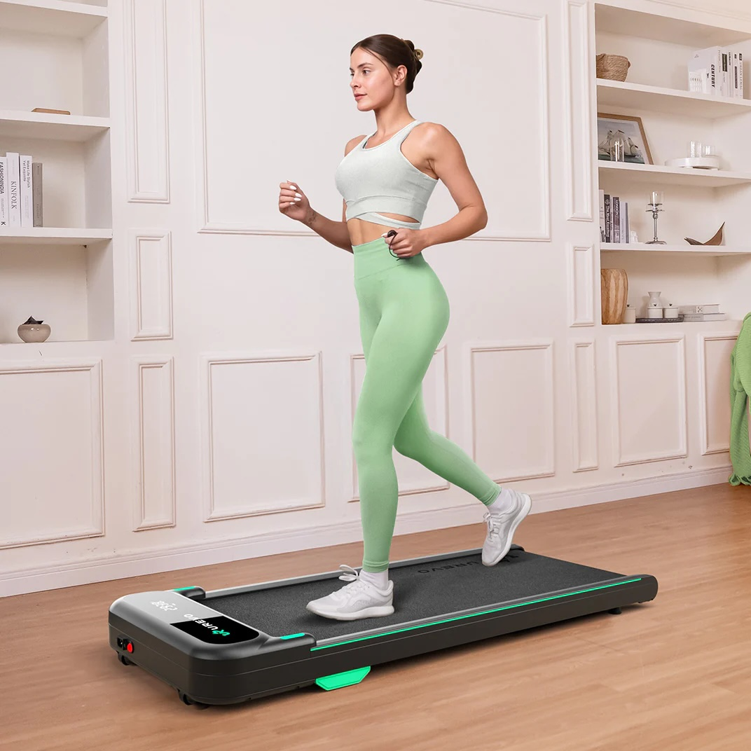 Kobieta w miętowo-zielonym stroju sportowym biegnie na bieżni w jasnym pomieszczeniu.