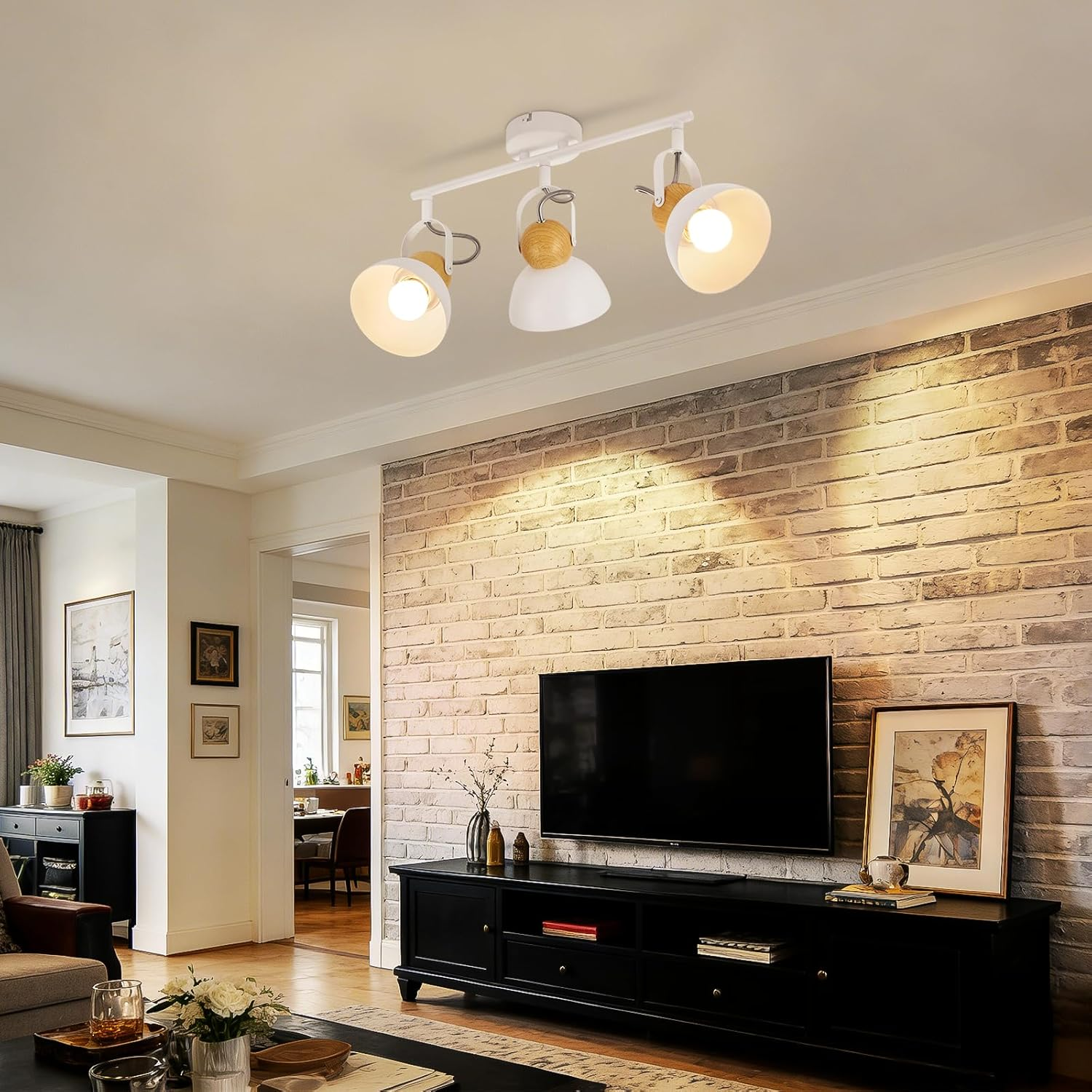 Trzyreflektorowe oświetlenie sufitowe nad czarną szafką RTV na tle ceglanej ściany.