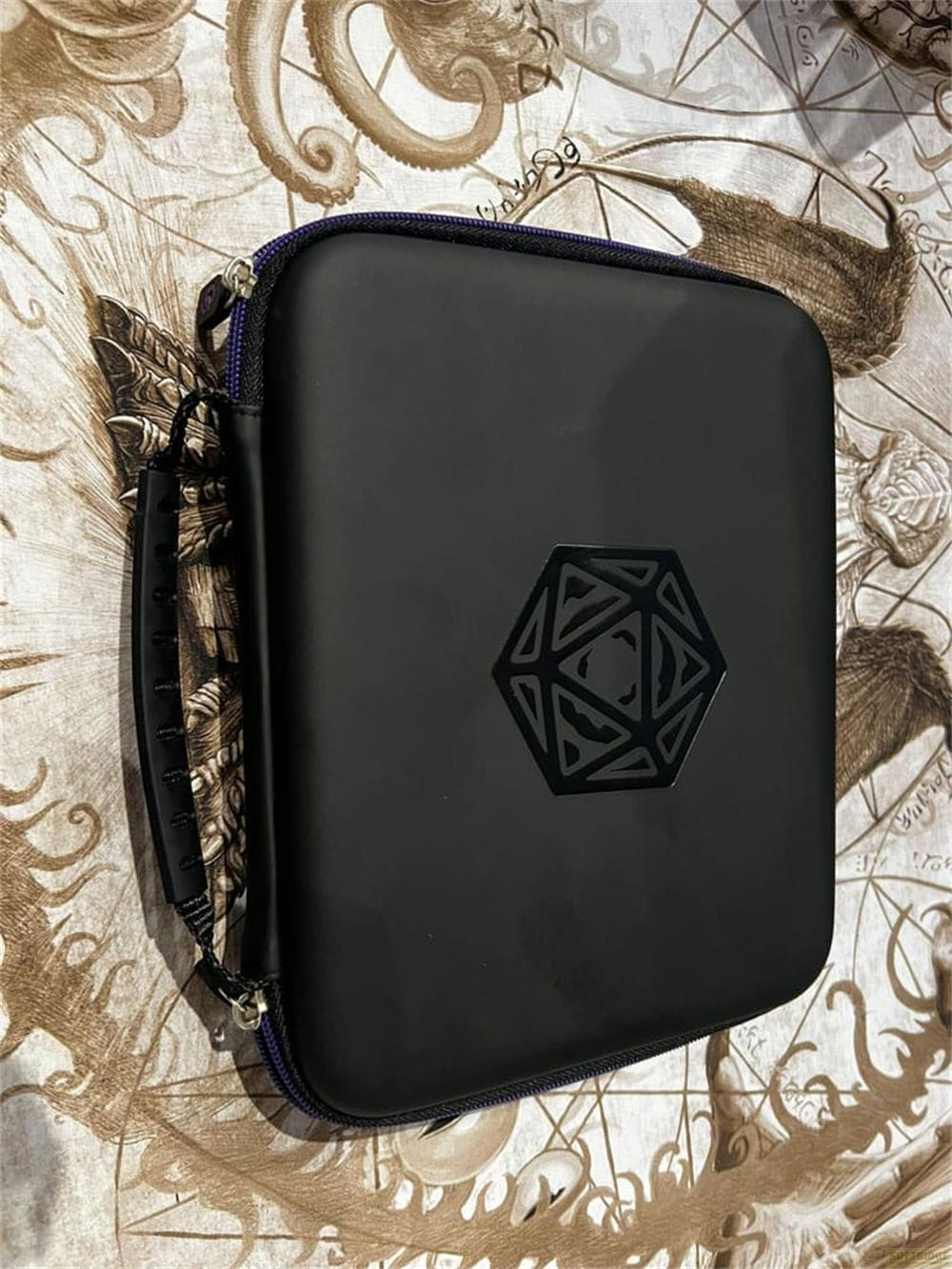Schwarze Tasche mit Würfelsymbol, liegt auf bedrucktem Stoff.