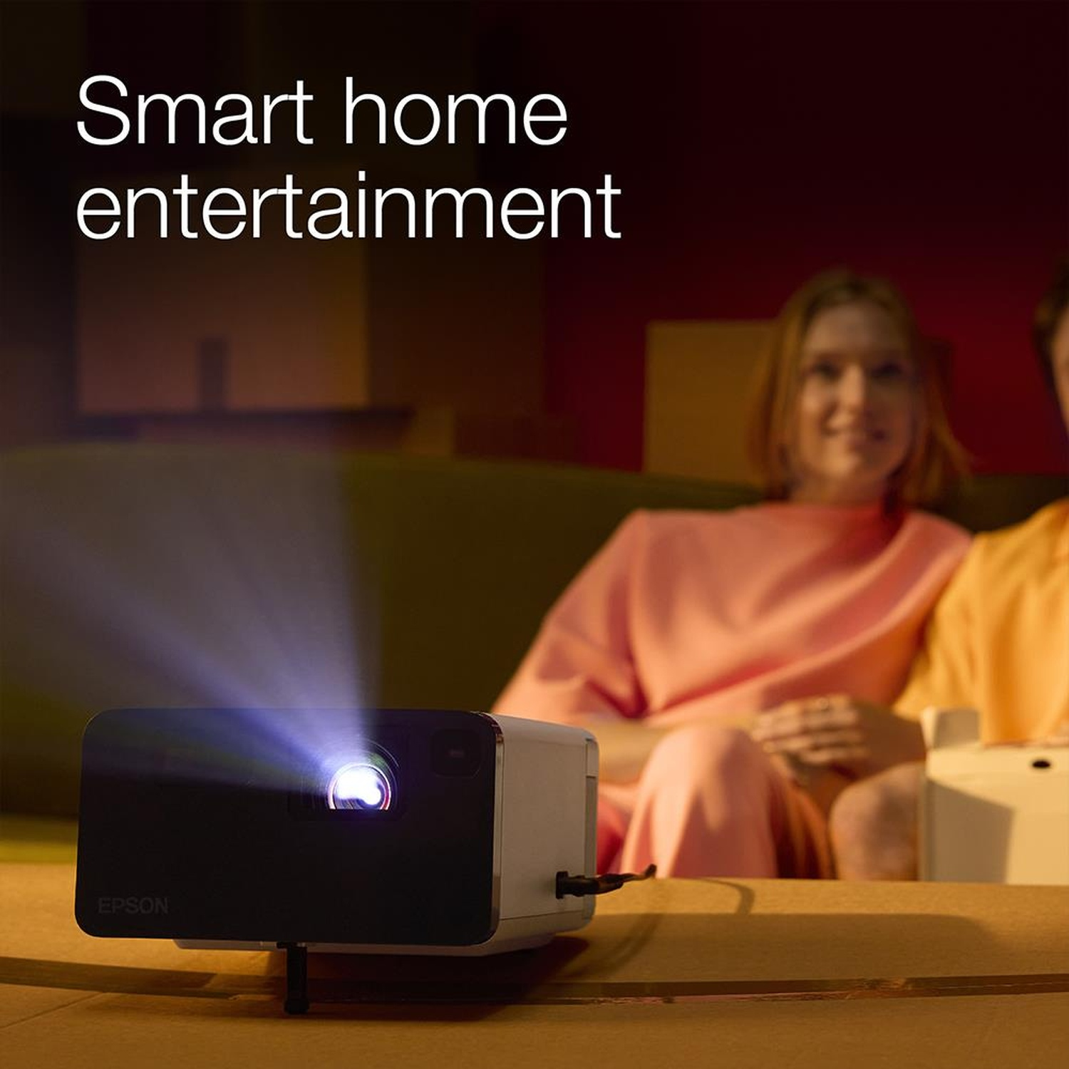 Ein Epson-Projektor strahlt Licht aus, während zwei Personen auf einem Sofa sitzen.