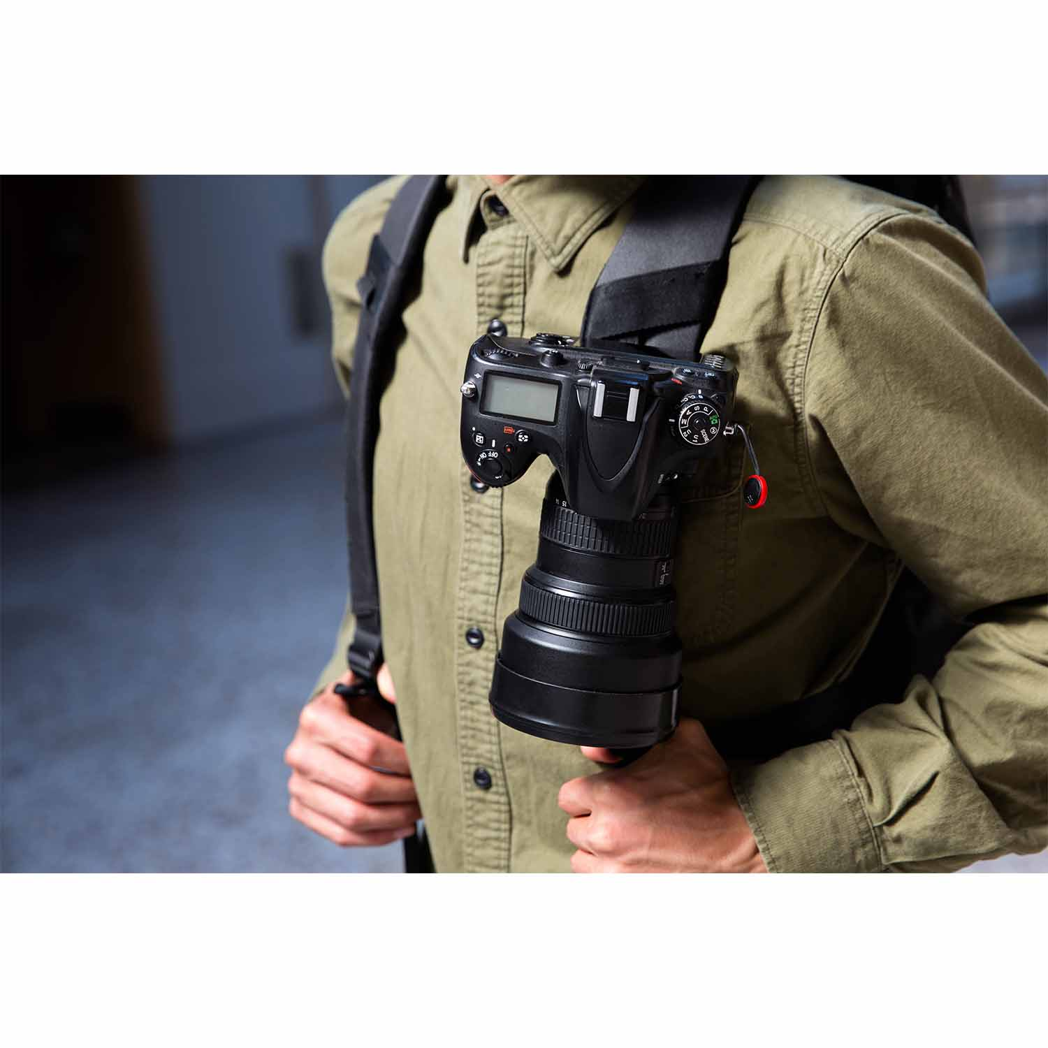 Una persona con camicia verde indossa una fotocamera con obiettivo sulla spalla.
