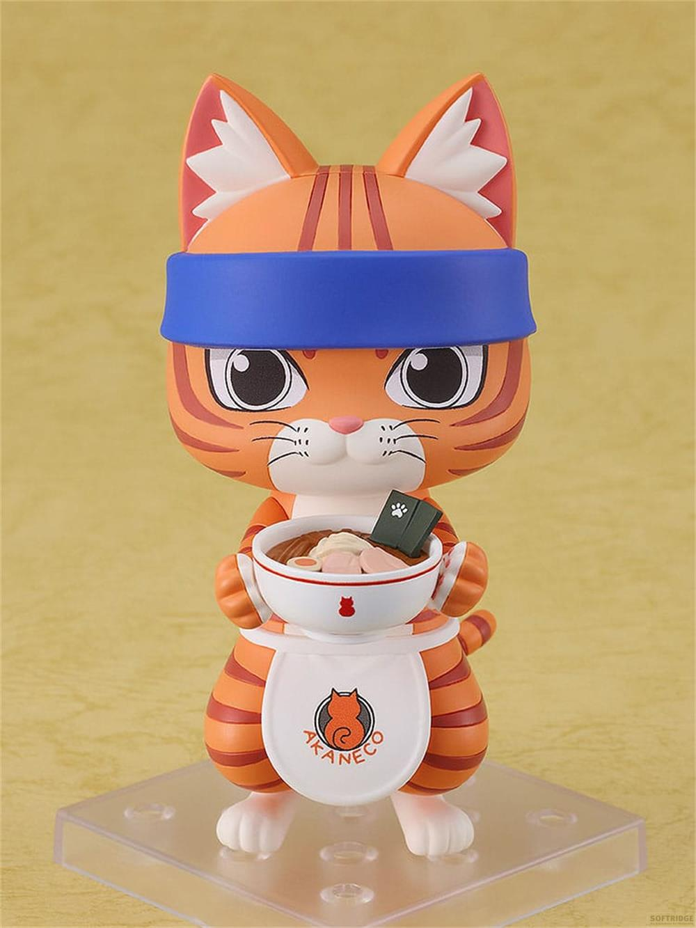 Eine orangefarbene Figur einer Katze mit blauer Stirnband und Latzschürze hält eine Schüssel Nudelsuppe.