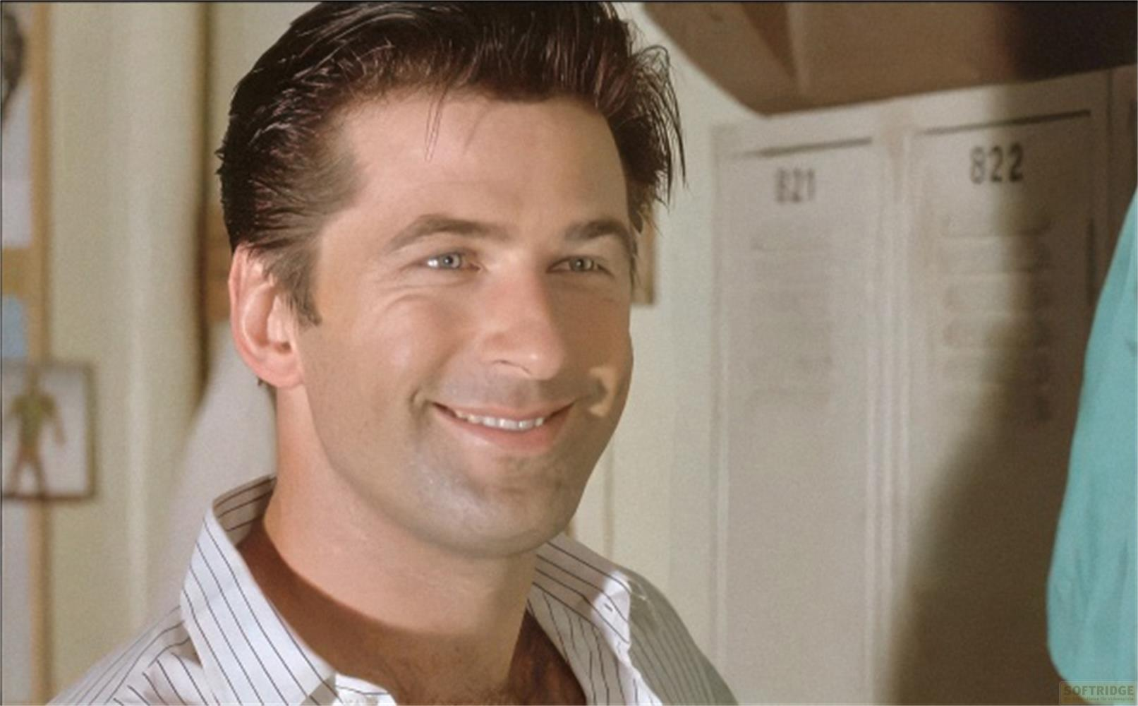 Un uomo con capelli scuri sorride, indossa una camicia a righe. Numeri di porta sullo sfondo.