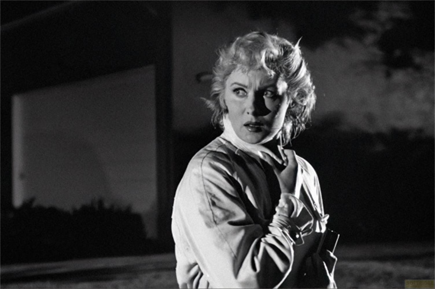 Donna con capelli biondi guarda a sinistra, indossa una camicia chiara, scena notturna.